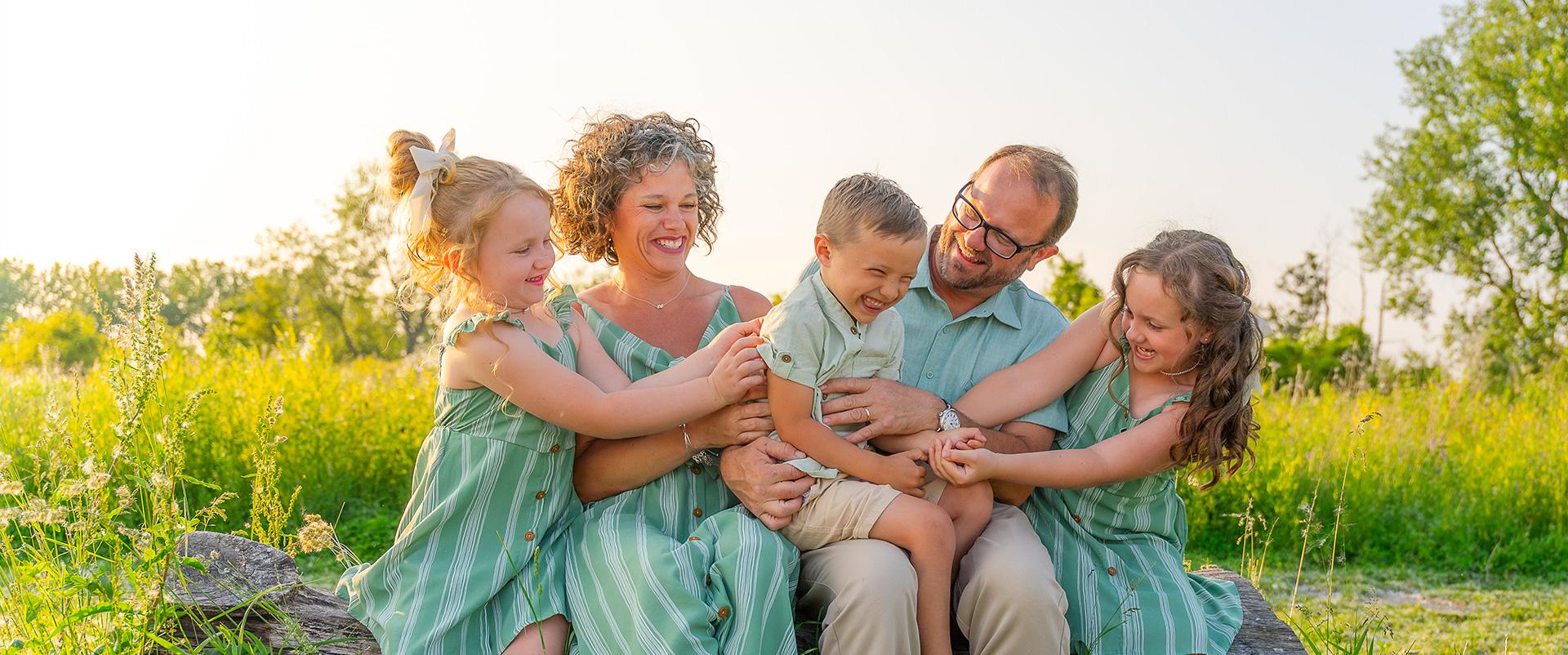 A family of five enjoying some tickles in a park at sunset.